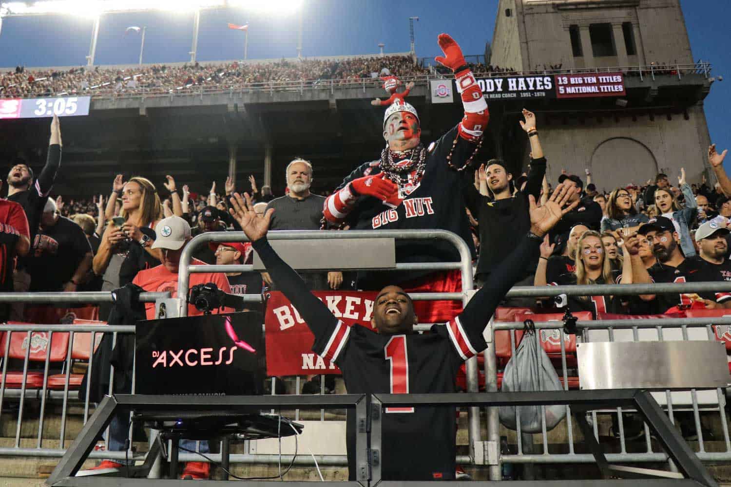 A cheering crowd at a sports event, with fans wearing team colors and one person in distinctive face paint and outfit, celebrating.