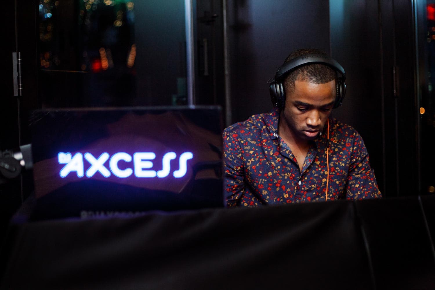 A man wearing headphones stands by a DJ booth with AXCESS illuminated on the screen.