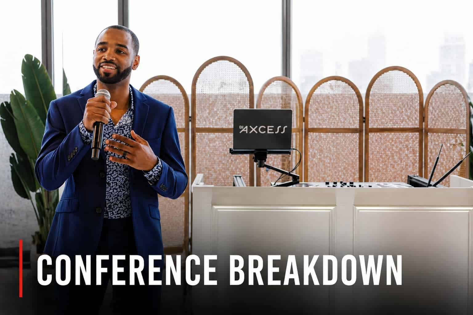 “DJ AXCESS speaking into a handheld microphone at a conference, standing in front of a DJ booth and AV setup, demonstrating live event production and MCing.”